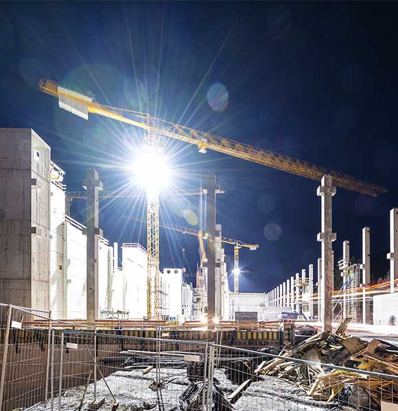 Floodlit tower crane on building construction site at night.