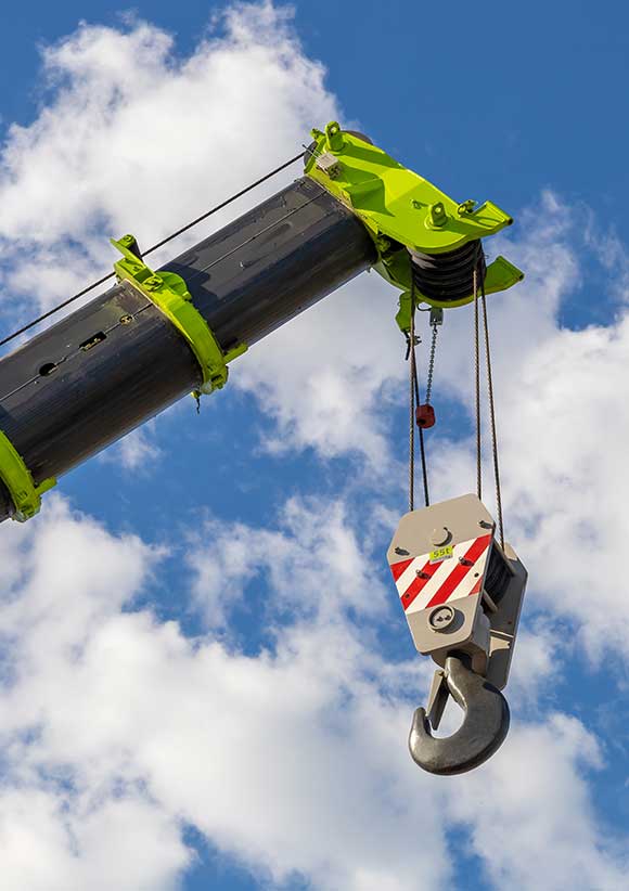 Telescopic boom of a mobile crane with a hook against a cloudy sky.
