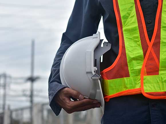 A construction worker in a blue jumpsuit holds a hat.