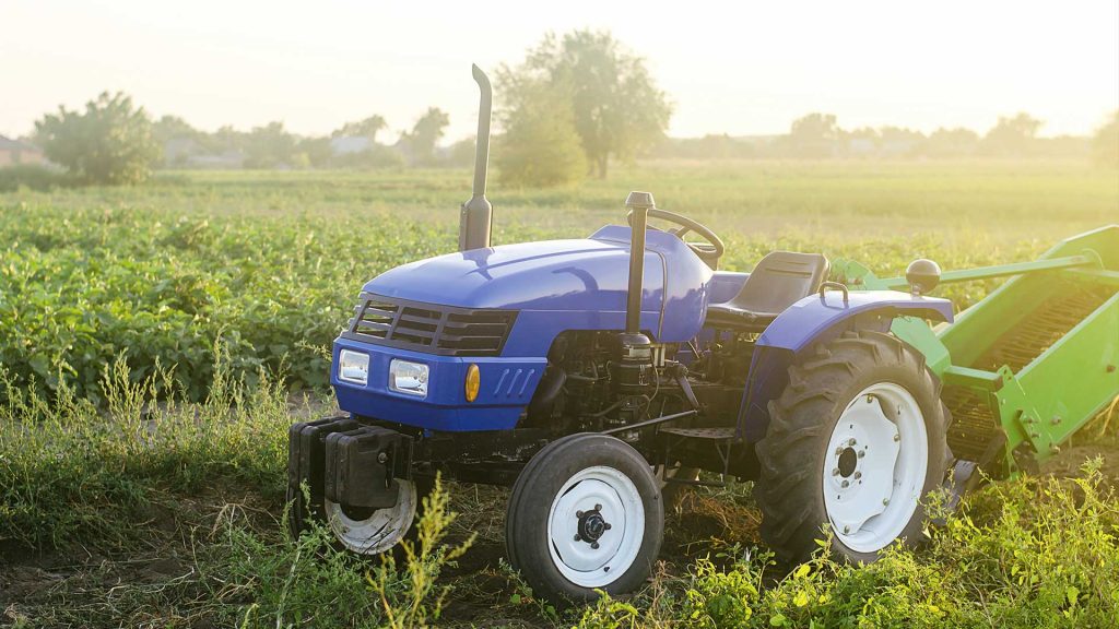 A blue tractor on the farm field The use of machines in agriculture increases the speed and efficiency of work. Farming and farmland Harvesting potatoes in the autumn countryside.