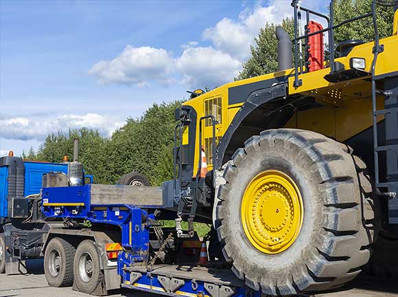 A blue trailer with heavy equipment loaded at the back.